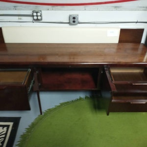 Pu&ograve; includere: Una scrivania in legno scuro con tre cassetti, di cui due sono aperti. La scrivania ha una superficie liscia e lucida ed &egrave; realizzata in legno di alta qualit&agrave;. La scrivania si trova in una stanza con un soffitto bianco e un tappeto verde.