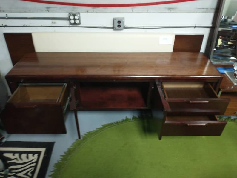 Pu&ograve; includere: Una scrivania in legno scuro con tre cassetti, di cui due sono aperti. La scrivania ha una superficie liscia e lucida ed &egrave; realizzata in legno di alta qualit&agrave;. La scrivania si trova in una stanza con un soffitto bianco e un tappeto verde.