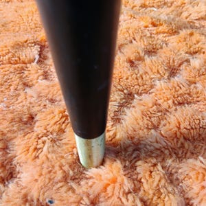 May include: A tapered furniture leg with a smooth black finish and a metallic gold-toned ferrule at the base. The leg is cylindrical in shape, narrowing slightly toward the bottom, and features a clean, polished transition between the black and gold.