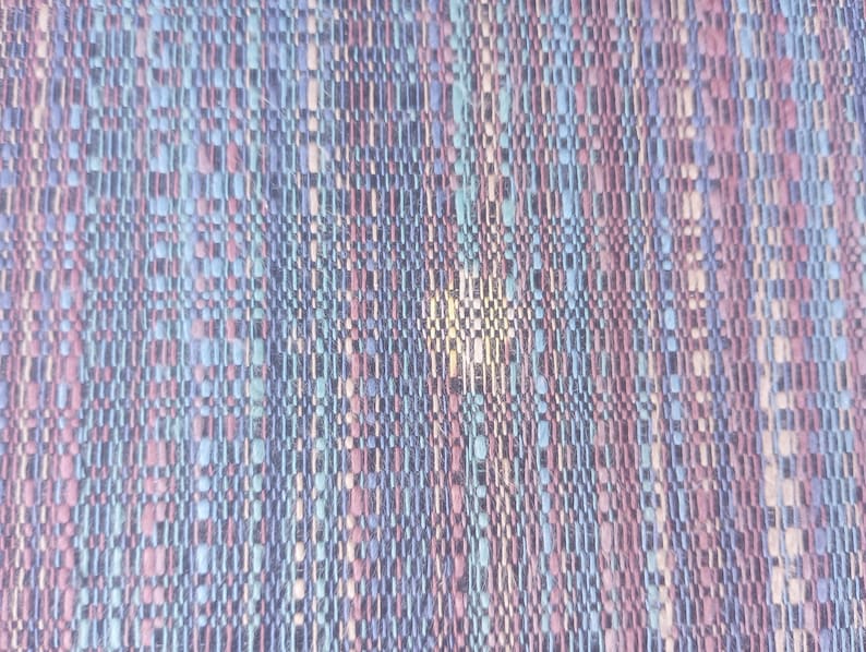 May include: A close-up of a woven fabric with a textured pattern in shades of blue, pink, and white.
