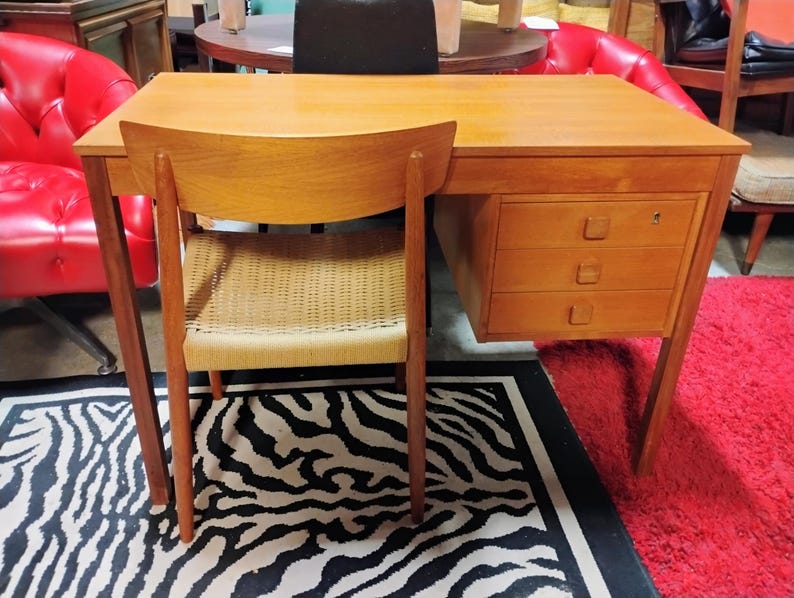 May include: A light brown wooden desk with three drawers and a matching chair. The chair has a woven seat. The desk and chair are set on a black and white zebra-print rug and a red rug.