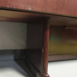 Pu&ograve; includere: Primo piano della parte inferiore di un armadio in legno scuro con una sola gamba visibile. La gamba &egrave; di colore marrone scuro e ha una forma arrotondata.