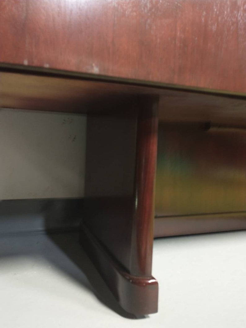 Pu&ograve; includere: Primo piano della parte inferiore di un armadio in legno scuro con una sola gamba visibile. La gamba &egrave; di colore marrone scuro e ha una forma arrotondata.