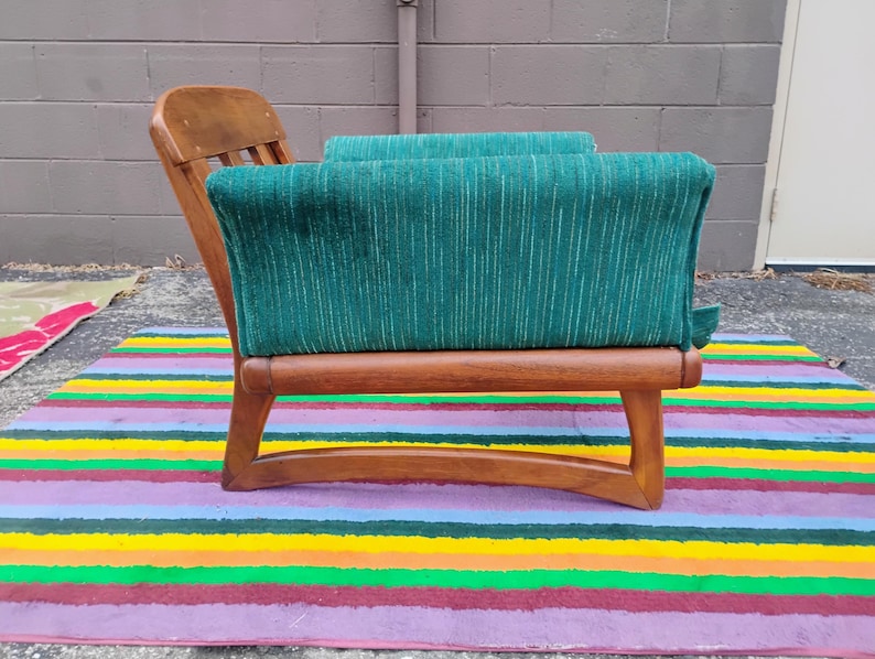 May include: A wooden armchair featuring a curved frame and a deep green upholstered seat and backrest. The fabric has a subtle vertical striped texture. The chair has a low-profile design with exposed wooden armrests and a slatted backrest.