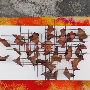 May include: A metal wall sculpture with a grid pattern and abstract shapes. The shapes are made of copper and have a reddish-brown color.