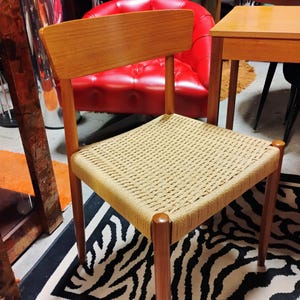 May include: A mid-century modern chair with a light brown wooden frame and backrest. The seat is woven with a light tan rope. The chair has four legs and is set on a black and white zebra-striped rug. The chair is a piece of furniture.