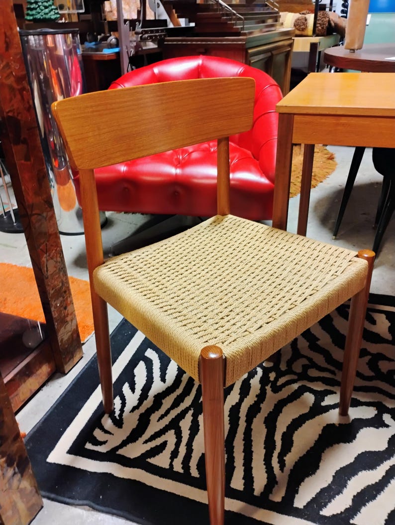 May include: A mid-century modern chair with a light brown wooden frame and backrest. The seat is woven with a light tan rope. The chair has four legs and is set on a black and white zebra-striped rug. The chair is a piece of furniture.