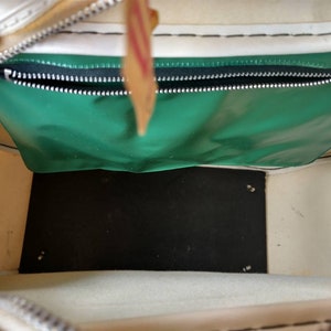 Pode incluir: Vista interna de uma bolsa de lona branca com um bolso com z&iacute;per verde e um fundo preto. A bolsa tem um z&iacute;per branco e costuras brancas.