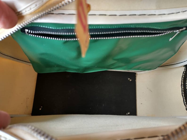 Pode incluir: Vista interna de uma bolsa de lona branca com um bolso com z&iacute;per verde e um fundo preto. A bolsa tem um z&iacute;per branco e costuras brancas.