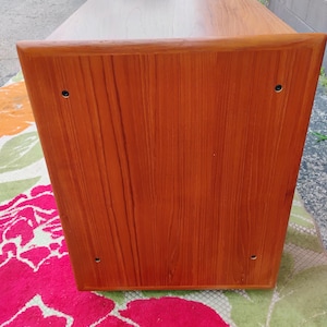 May include: A rectangular wooden console table with a warm brown finish and visible wood grain. The side panel features four small, dark circular screw covers positioned near each corner, and the top surface extends slightly beyond the side edge.