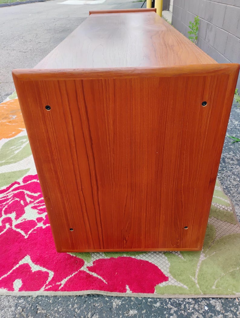 May include: A rectangular wooden console table with a warm brown finish and visible wood grain. The side panel features four small, dark circular screw covers positioned near each corner, and the top surface extends slightly beyond the side edge.