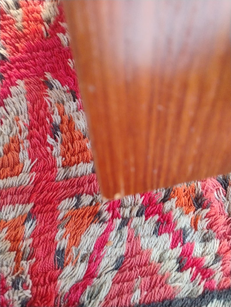 May include: Close-up of a wooden object with a warm, reddish-brown hue. The wood grain is visible. The object is set against a colorful rug with a pattern of red, orange, white, and gray.