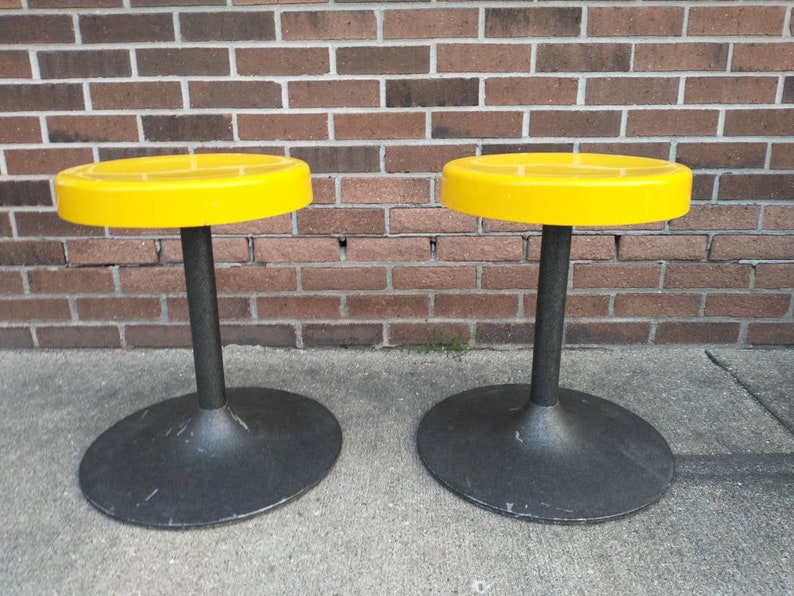 May include: Two yellow round stools with black bases. The stools are made of plastic and have a simple, modern design.