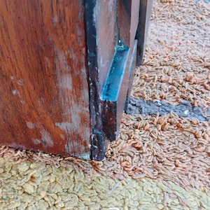 Puede incluir: Primer plano de un objeto de madera con un rico tono marr&oacute;n rojizo, que muestra la veta de la madera visible y signos de desgaste. Una secci&oacute;n del objeto tiene un acento azul. El objeto est&aacute; sobre una superficie texturizada y multicolor.