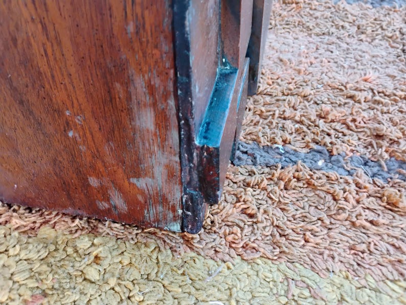 Puede incluir: Primer plano de un objeto de madera con un rico tono marr&oacute;n rojizo, que muestra la veta de la madera visible y signos de desgaste. Una secci&oacute;n del objeto tiene un acento azul. El objeto est&aacute; sobre una superficie texturizada y multicolor.