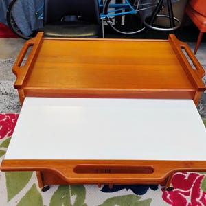 May include: A wooden serving cart with a white top and two handles. The cart has a lower shelf and wheels.