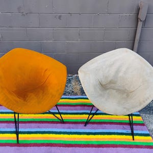 May include: Two diamond-shaped chairs with thin black metal legs. One chair is upholstered in a vibrant mustard yellow fabric, while the other is covered in a light beige material. Both chairs feature a wide, angular seat design.
