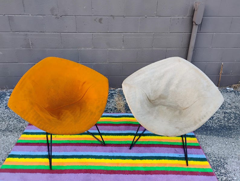 May include: Two diamond-shaped chairs with thin black metal legs. One chair is upholstered in a vibrant mustard yellow fabric, while the other is covered in a light beige material. Both chairs feature a wide, angular seat design.