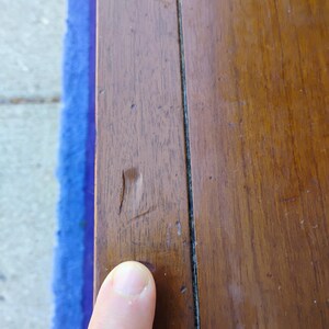 May include: Close-up of a dark brown wooden surface with a visible crack and a thin black line running down the center.
