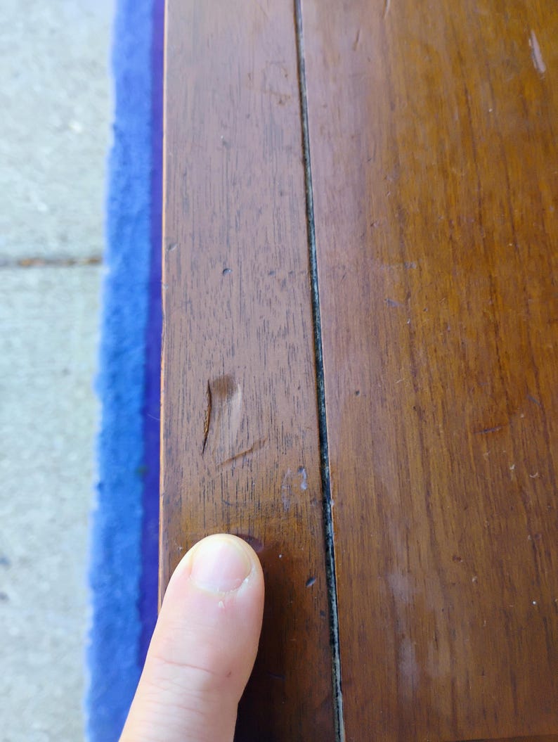 May include: Close-up of a dark brown wooden surface with a visible crack and a thin black line running down the center.