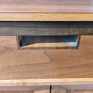 Op de afbeelding: Een houten ladefront met een horizontaal nerfpatroon in een medium bruine tint. De lade is voorzien van een rechthoekige verzonken handgreep die direct in het midden van het houten paneel is ge&iuml;ntegreerd, onder een platte bovenrand.