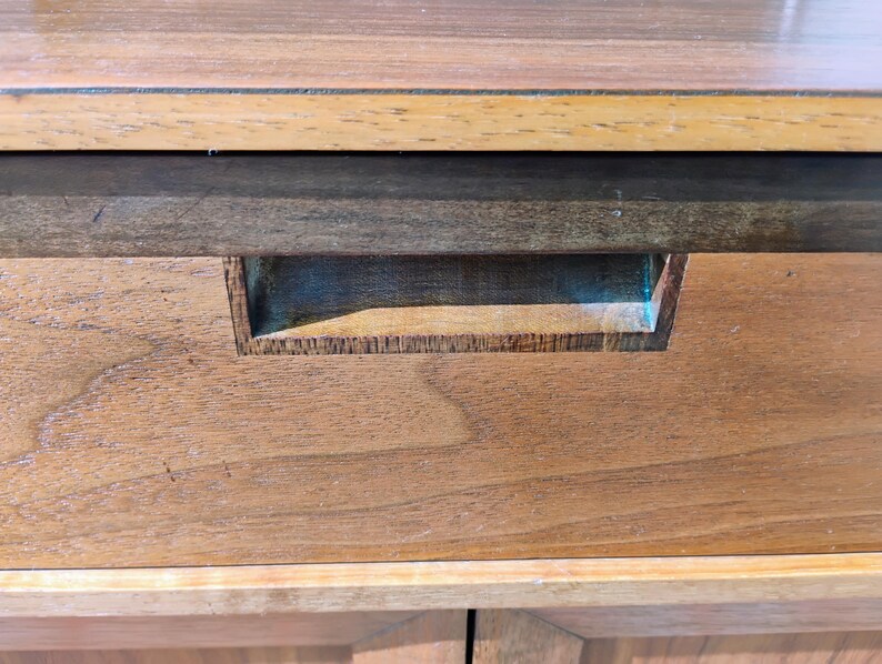 Op de afbeelding: Een houten ladefront met een horizontaal nerfpatroon in een medium bruine tint. De lade is voorzien van een rechthoekige verzonken handgreep die direct in het midden van het houten paneel is ge&iuml;ntegreerd, onder een platte bovenrand.