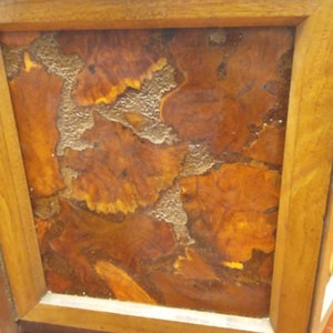 May include: Close-up of a wooden box with a framed design. The design features a mosaic of brown and orange wood pieces with a textured, light-colored filler. The frame is made of light brown wood.