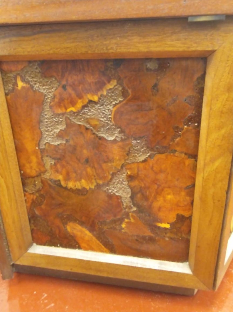 May include: Close-up of a wooden box with a framed design. The design features a mosaic of brown and orange wood pieces with a textured, light-colored filler. The frame is made of light brown wood.