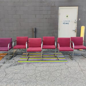 May include: A set of six cantilever chairs with polished chrome metal frames and upholstered seats and backrests in varying shades of red and magenta. Each chair features a continuous tubular metal base and integrated armrests with black caps.