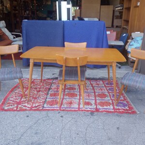 May include: A set of four mid-century modern dining chairs with a wood frame and patterned fabric seats surrounding a rectangular wood table with tapered legs. The chairs and table are on a red and purple patterned rug.
