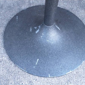 May include: A close-up of the bottom of a gray metal table base. The base is round and has a slightly flared edge. The base is marked with the word "Made in Japan".