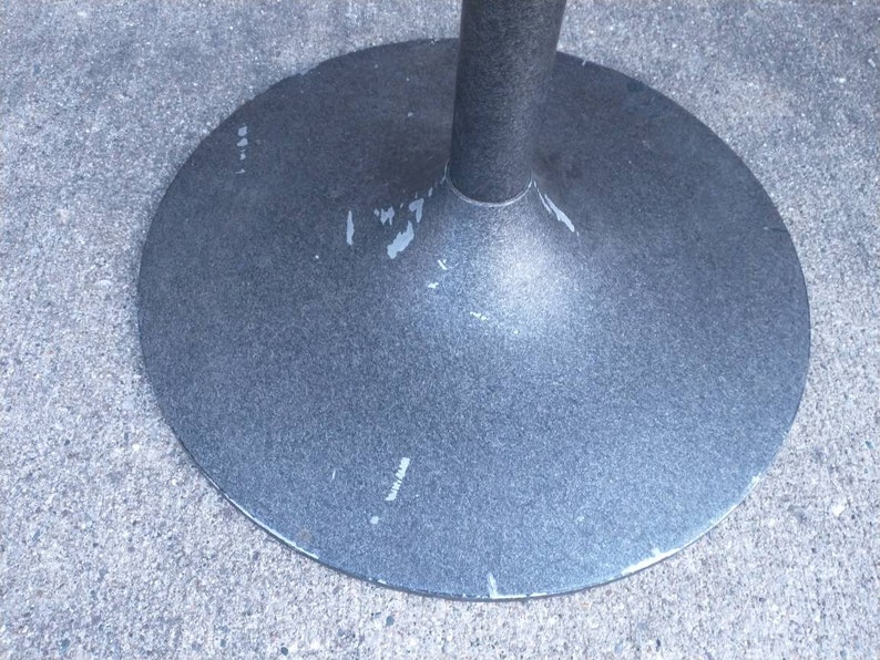 May include: A close-up of the bottom of a gray metal table base. The base is round and has a slightly flared edge. The base is marked with the word "Made in Japan".