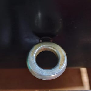 May include: A close-up shot of a metal eye bolt with a circular eye. The eye bolt is silver and has a circular opening in the center. The background is dark and out of focus.