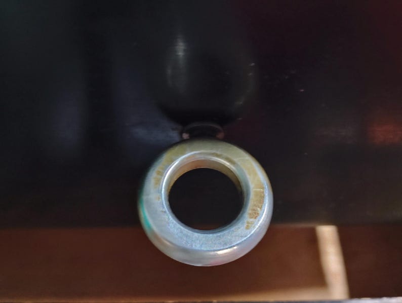 May include: A close-up shot of a metal eye bolt with a circular eye. The eye bolt is silver and has a circular opening in the center. The background is dark and out of focus.