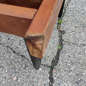 K&ouml;nnte beinhalten: Nahaufnahme eines Holzstuhls mit brauner Sitzfl&auml;che und schwarzen Beinen. Der Rahmen des Stuhls ist aus Holz gefertigt und die Beine sind schwarz lackiert. Der Stuhl scheint Vintage oder antik zu sein, mit sichtbaren Gebrauchsspuren.