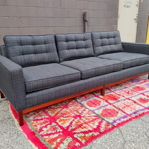 K&ouml;nnte beinhalten: Ein Dreisitzer-Sofa, bezogen mit einem dunkelgrauen, strukturierten Stoff mit einem dezenten Karomuster. Das Sofa verf&uuml;gt &uuml;ber drei getuftete R&uuml;ckenkissen, drei Sitzkissen und einen h&ouml;lzernen Unterbau mit geraden Beinen f&uuml;r eine klare Form.