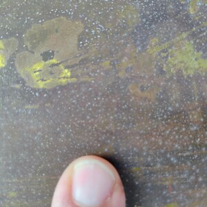 K&ouml;nnte beinhalten: Nahaufnahme einer strukturierten Oberfl&auml;che mit marmoriertem Aussehen. Die Oberfl&auml;che hat eine Mischung aus braunen, gelben und wei&szlig;en Farben mit einem gesprenkelten Muster. Die Textur wirkt rau und gealtert, mit einem Finger im Vordergrund.
