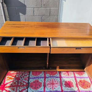 Op de afbeelding: Een rechthoekig houten dressoir met een warme bruine afwerking, voorzien van twee bovenste lades en twee onderste kastdeuren. De linkerlade bevat verdelers met een donkere stoffen voering, terwijl de rechterlade open en leeg is.