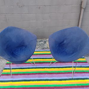 May include: Two matching chairs featuring deep blue fabric upholstery with a rounded, shell-like seat design. Each chair is supported by four thin, angled metal legs that provide a stable base for the curved, molded seat structure.