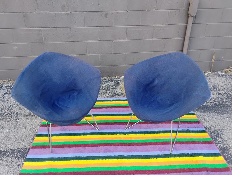 May include: Two matching chairs featuring deep blue fabric upholstery with a rounded, shell-like seat design. Each chair is supported by four thin, angled metal legs that provide a stable base for the curved, molded seat structure.