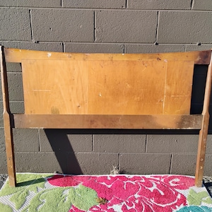 May include: A wooden headboard with a curved top and a simple design. The headboard is made of light brown wood and has a natural finish.