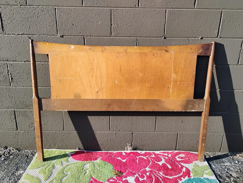May include: A wooden headboard with a curved top and a simple design. The headboard is made of light brown wood and has a natural finish.