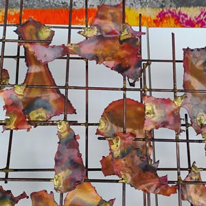 May include: Abstract wall art featuring a grid of metal with irregular, fragmented pieces of copper-toned metal with red and gold accents.