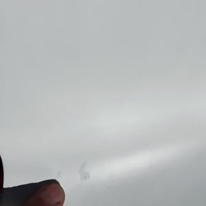 K&ouml;nnte beinhalten: Nahaufnahme einer wei&szlig;en Oberfl&auml;che mit ein paar kleinen, unregelm&auml;&szlig;igen, hellfarbigen Flecken. Der Rand eines dunklen Objekts ist auf der linken Seite des Bildes zu sehen, und ein Finger ist teilweise unten sichtbar.