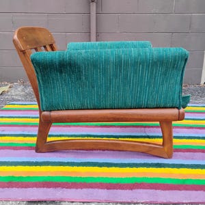 May include: A wooden armchair featuring a curved frame and a deep green upholstered seat and backrest. The fabric has a subtle vertical striped texture. The chair has a low-profile design with exposed wooden armrests and a slatted backrest.