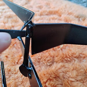 May include: Close-up of a black metal object with angular, geometric shapes. The object appears to be constructed from flat, welded pieces, with a matte finish. The design includes a central point with radiating arms.
