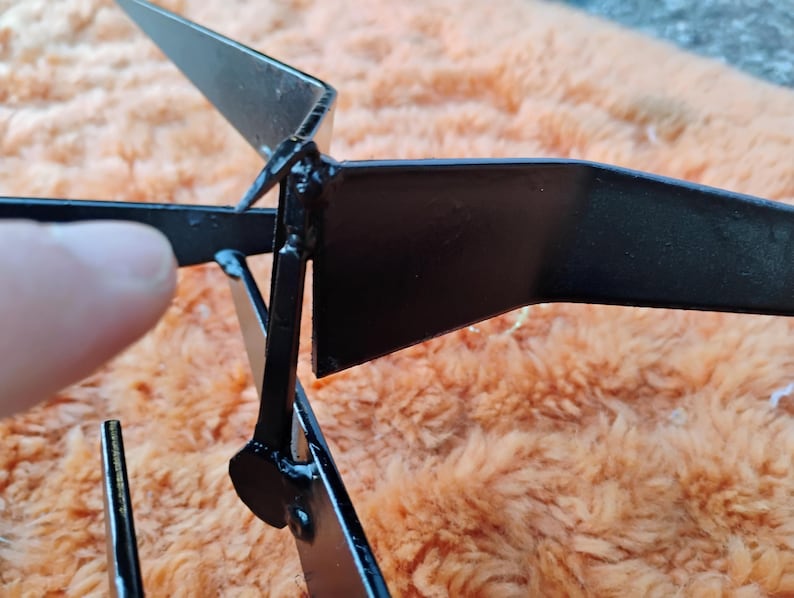 May include: Close-up of a black metal object with angular, geometric shapes. The object appears to be constructed from flat, welded pieces, with a matte finish. The design includes a central point with radiating arms.