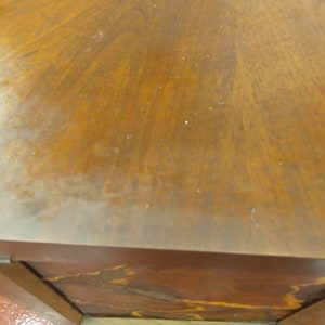 May include: Close-up of a wooden table with a rich, warm brown finish. The wood grain is visible, creating a natural pattern across the surface. The table's edge and corner are also visible, showing the construction and design.