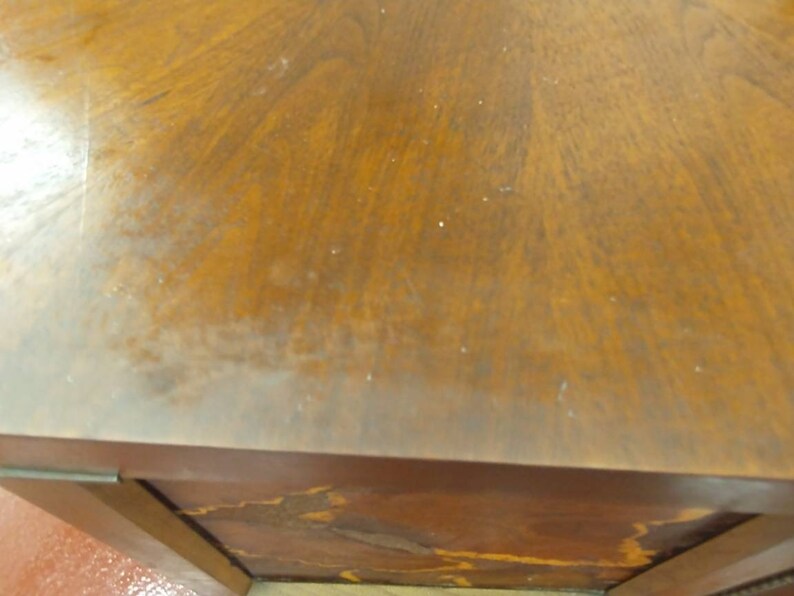 May include: Close-up of a wooden table with a rich, warm brown finish. The wood grain is visible, creating a natural pattern across the surface. The table's edge and corner are also visible, showing the construction and design.