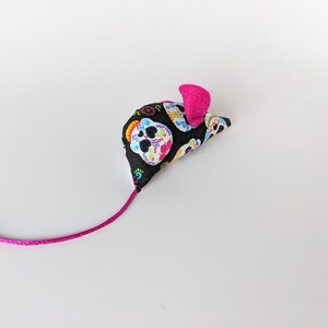 May include: A pink and black cat toy shaped like a mouse with a colorful sugar skull pattern.